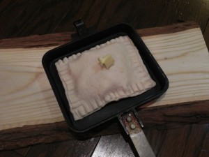 パイ生地（冷凍のパイ生地シートを使用）を伸ばして、底面はふくらまないよう穴をあける（上面はふくらむよう穴をあけない）。煮たリンゴを適当数入れたら、四方をフォークの背で綴じる。バターを塗ったホットサンドメーカーに入れ、上にもバターをのせる。 